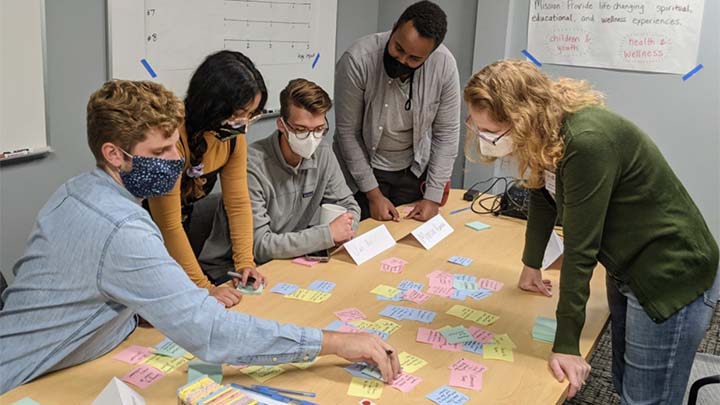 Five people seated and standing around a table review dozens of sticky notes.