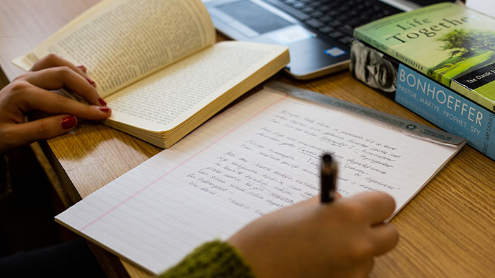 A student writing on a notepad in Turkish with copies of Dietrich Bonhoeffer's works next to her.