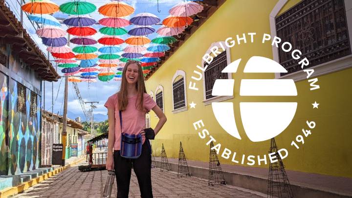 A female student stands on a brick road with colorful umbrellas hanging above her.