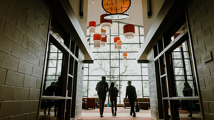 Three people with briefcases and bookbags walk away into a well-lit lobby area.