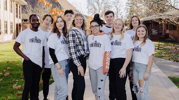 Ten students wearing "I'm First" shirts pose for a photo outside on Calvin's campus.