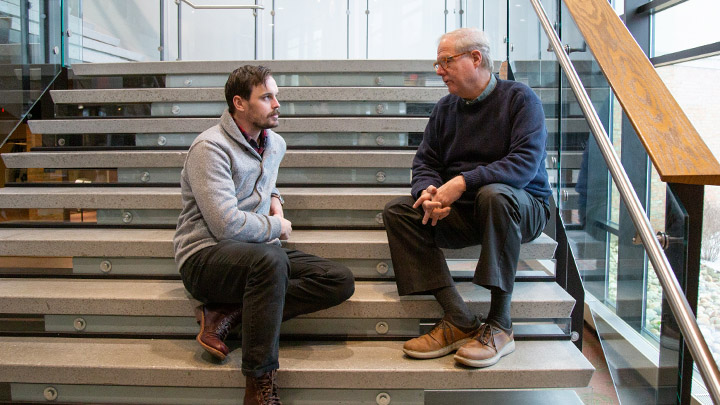 Two men seated on steps talking to one another.