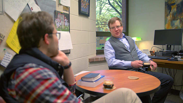 A business professor and a student having a discussion in an office setting.