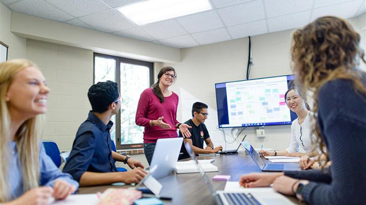 A female professor teaching a handful of students in a business class.