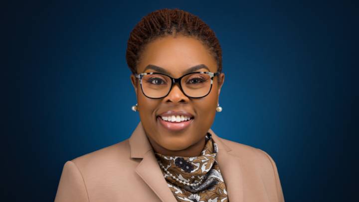 A smiling woman in glasses a suit coat and scarf.