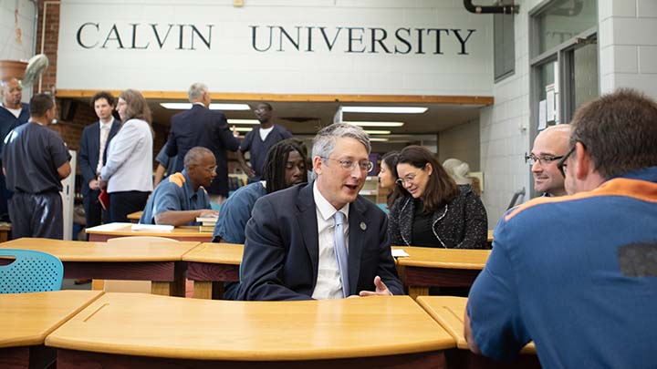 A classroom setting with inmates talking to leaders in suits and ties.