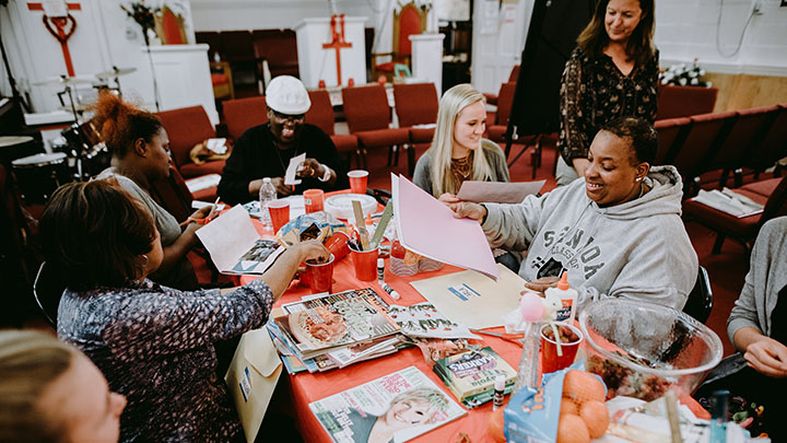 Women sitting around a rectangular table are working on an art project.