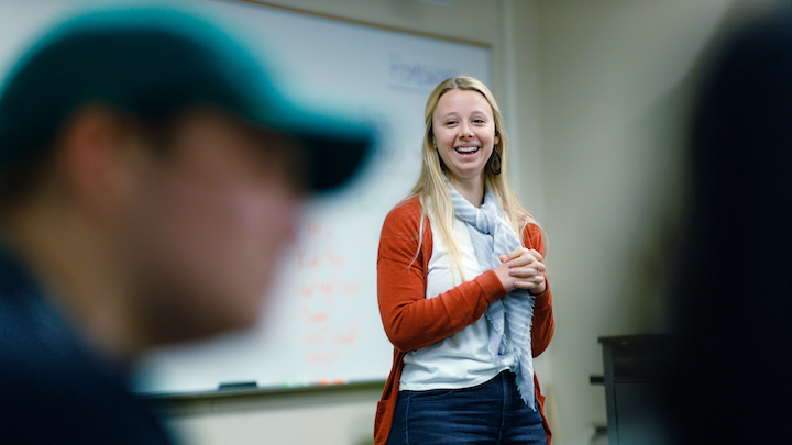 A student standing and smiling at the front of class.