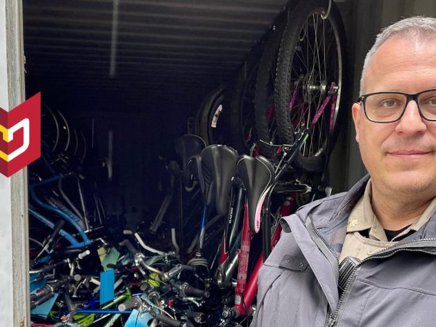 Tyson Moore stands in police uniform in front of stack of bikes