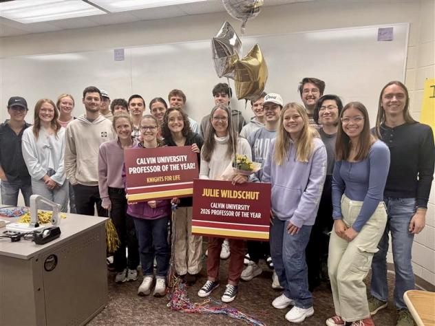 Julie Wildschut is surrounded by students in her classroom, holding professor of the year signs and balloons.