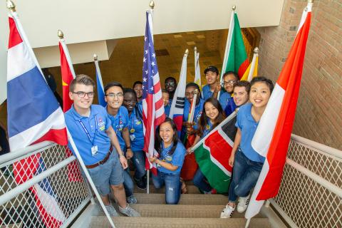 Calvin University international students standing with country flags in a stairwell looking up at the camera