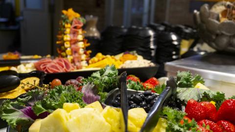 A fancy spread of various fruits, and an intricate tower of cold cut meats and cheeses.