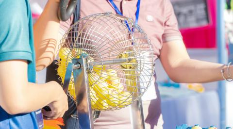 Two individuals standing next to a Bingo Cage filled with numbered yellow balls