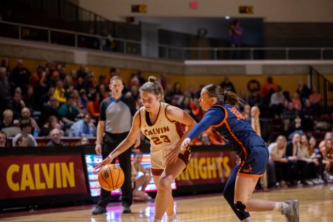 A Calvin women's basketball player dribbles down the court with a Hope College defender.