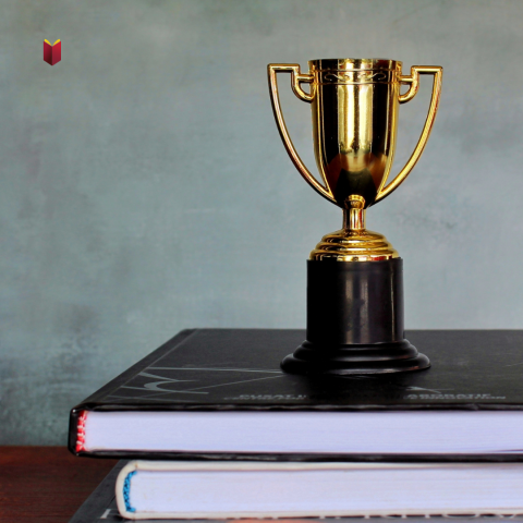 Mini trophy set atop a stack of books - Hekman Library logo in corner