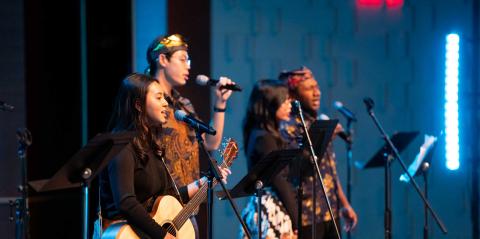 A diverse group of students leads worship with singing and guitar.