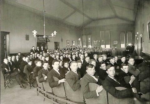 An old photo of a group of students, all males wearing suits, seated for a class.