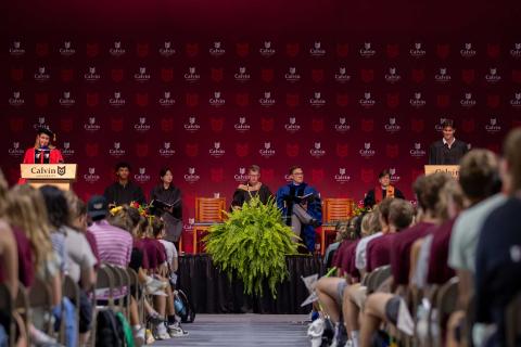 Leaders of Calvin University sit on the stage at opening convocation while the student body president gives and address, and incoming students fill the seats.