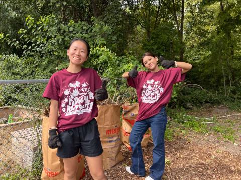 Two new Calvin students in maroon streetfest shirts give thumbs up while doing landscaping work.