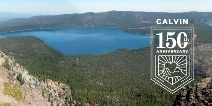 View from above of a lake surrounded by evergreen forests and cliffs, with the Calvin 150th anniversary logo overlay.