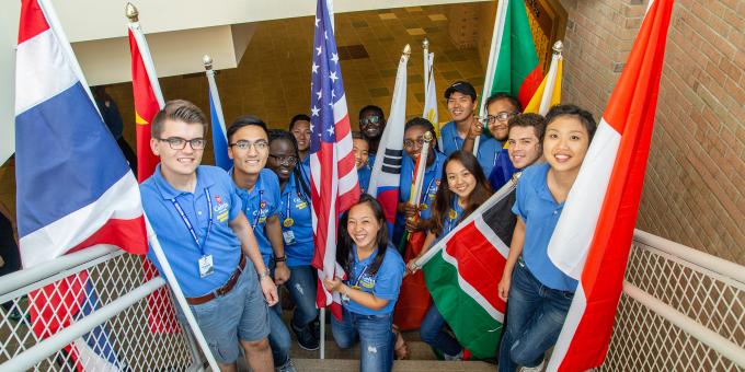 Calvin University international students standing with country flags in a stairwell looking up at the camera