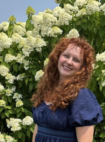 Jessi Galligan in a blue dress standing in front of hydrangea bushes in full bloom