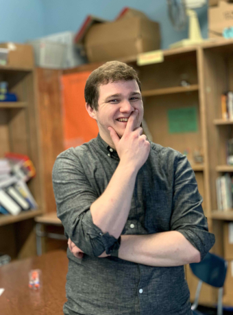 Nathan Stripp standing in his classroom in a gray button down shirt