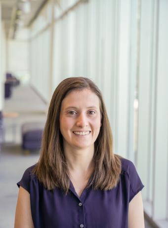 Jessica Thayer standing in a dark purple short-sleeved shirt with a blurred light background