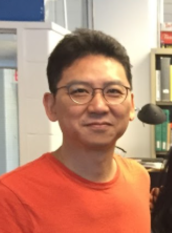 Junmo Cho looking at the camera - a man with glasses and an orange shirt