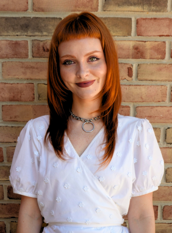 Woman with red hair standing in front of brick wall. 
