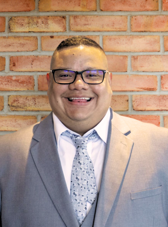 Man with glasses in front of brick wall. 