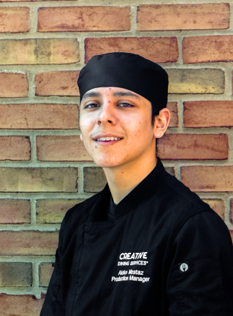 Man in a chef's hat in front of a brick wall.