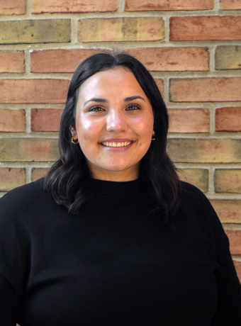 Woman in black shirt with brown hair smiling in front of a brick wall.