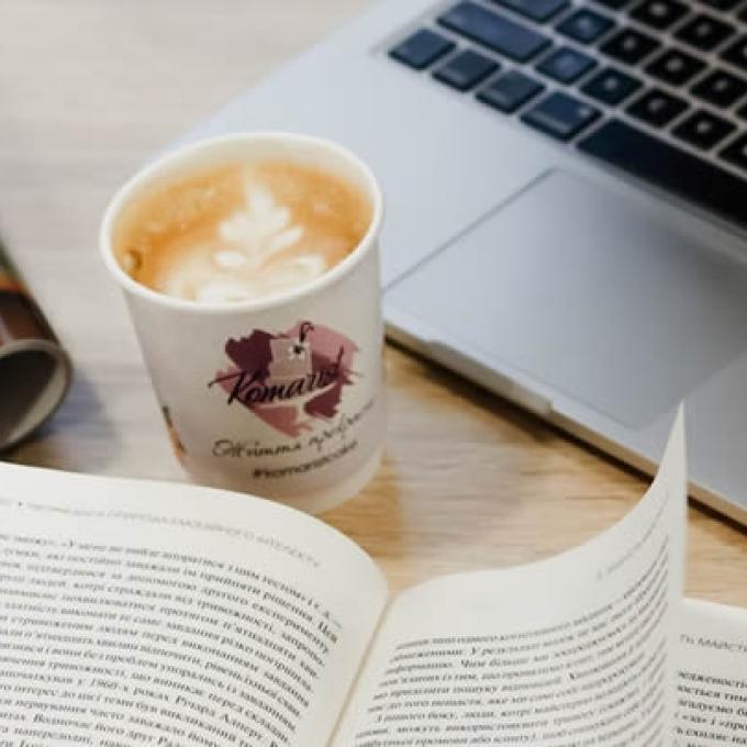 A cup of coffee in front of a laptop with an open book in the foreground