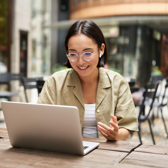 Young woman with glasses on sitting outside at a cafe on a laptop