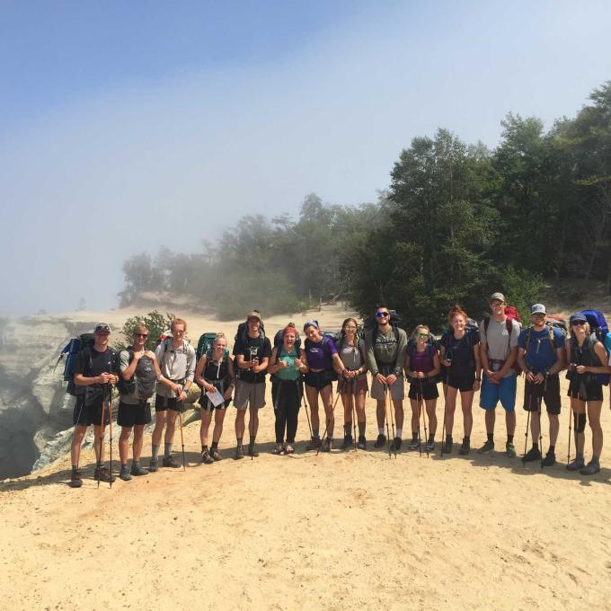 A large group of backpacking students stands near a cliff at the Pictured Rocks.