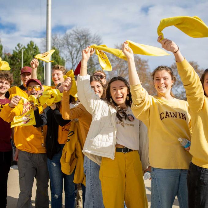 Calvin students all wearing maroon and gold Calvin gear wave towels in the air, cheering.