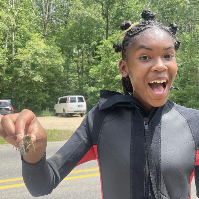 A student in a wetsuit smiles excitedly with a crayfish in her hand