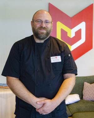 Man in a black chef coat poses for a photo