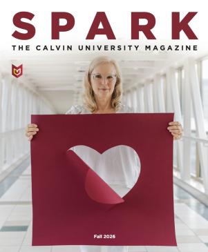 Julie Yonker, a Calvin professor, hold a large maroon poster with a heart cut out of it.