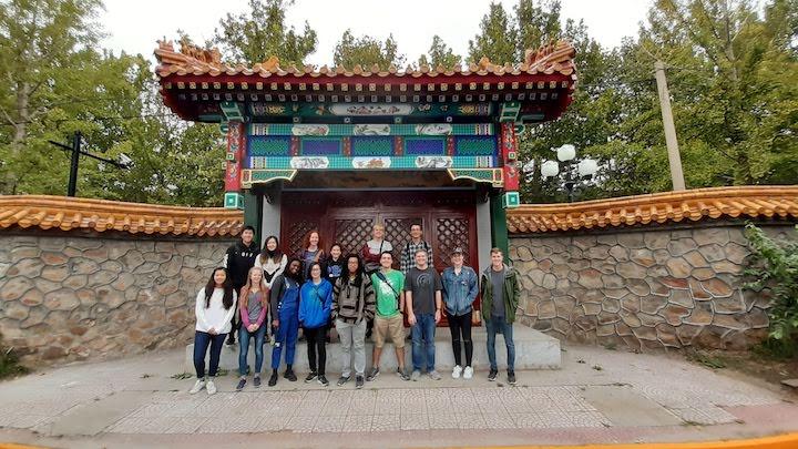 A group of students stand in front of a Chinese landmark.