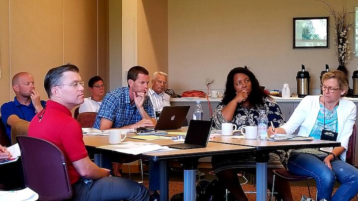 Adults gathered around a classroom table, with laptops and coffee mugs, attending an executive course.