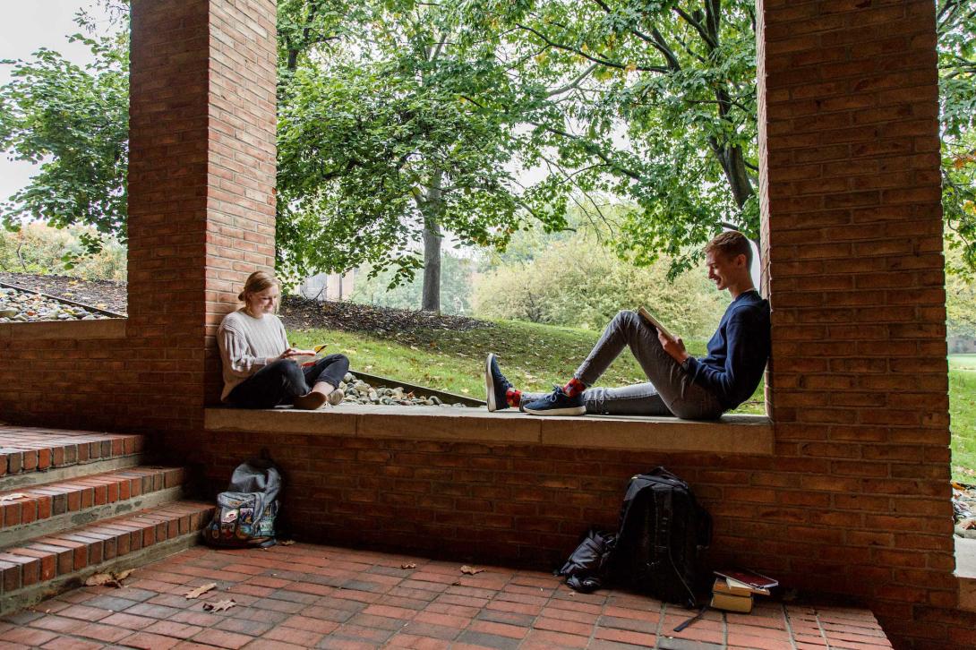 Two students sit on a brick wall working on school work.