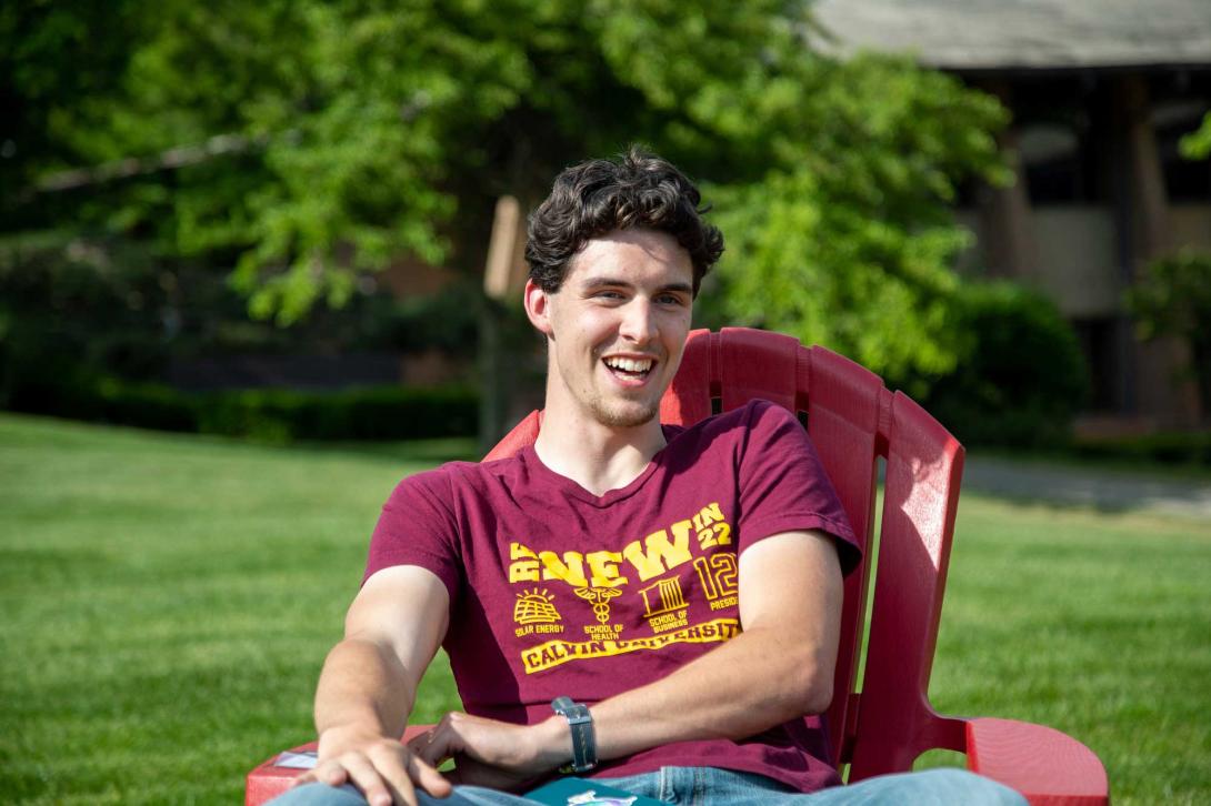 A male student sits in a chair on the green Calvin commons lawn.