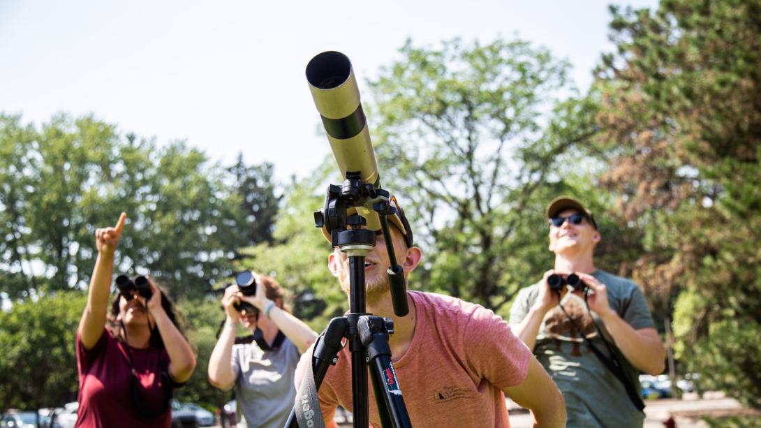 Four people looking through binoculars and a telescope
