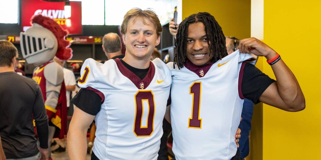 Two Calvin football players pose in their jerseys, with Joust the knight mascot in the background.