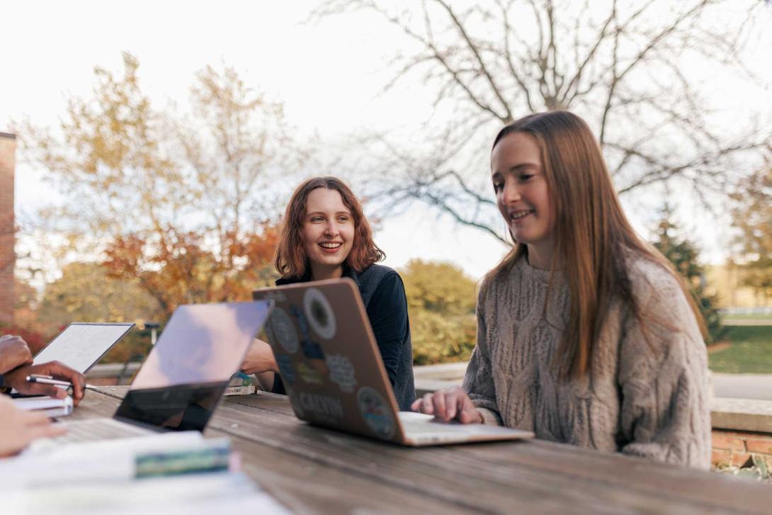 Two students work on laptops on a picnic table on Calvin's campus.