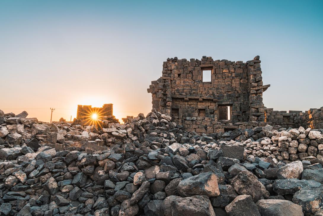 A picture of a building ruin with rocks surrounding it and the sunset behind the ruins