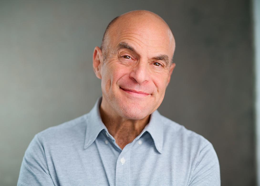 Peter, a white male who is bald, smirks for a professional headshot wearing a blue button up shirt.