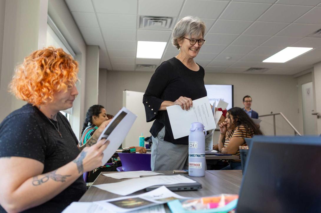 A Calvin University Wayfinder student works at a desk while a professor looks on.